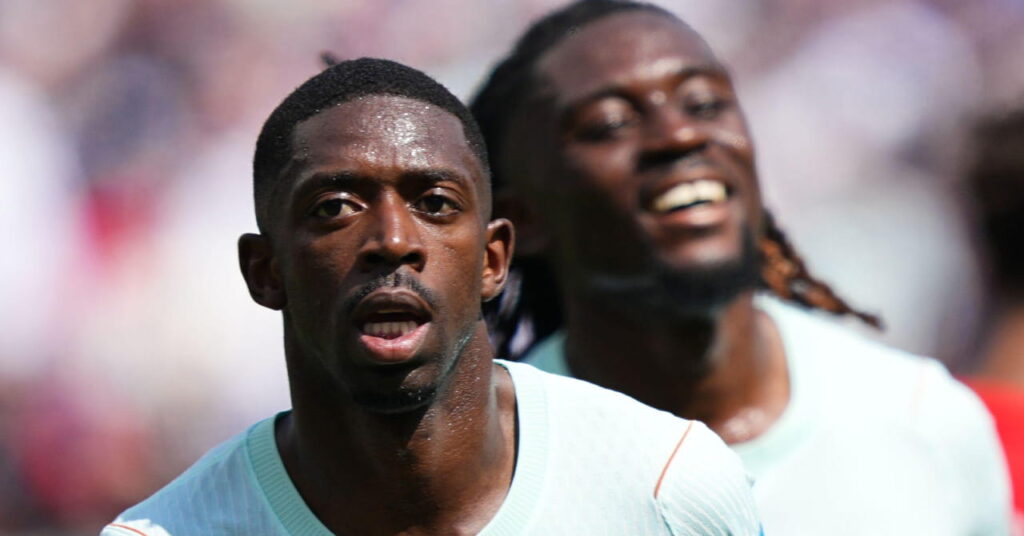 Footballer Ousmane Dembele running to celebrate a goal on a pitch while wearing a white France national football team shirt with a smiling teammate blurrily visible behind him at the World Cup 2026