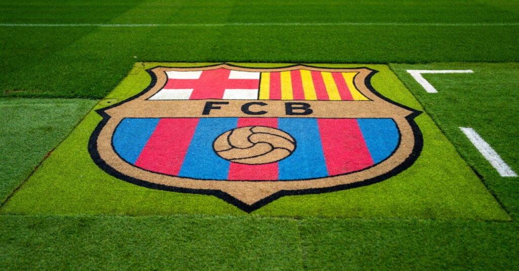 The Camp Nou stadium home of La Liga team Barcelona Football Club in day light with a green pitch and an emblem of the red and blue and yellow club badge marked out