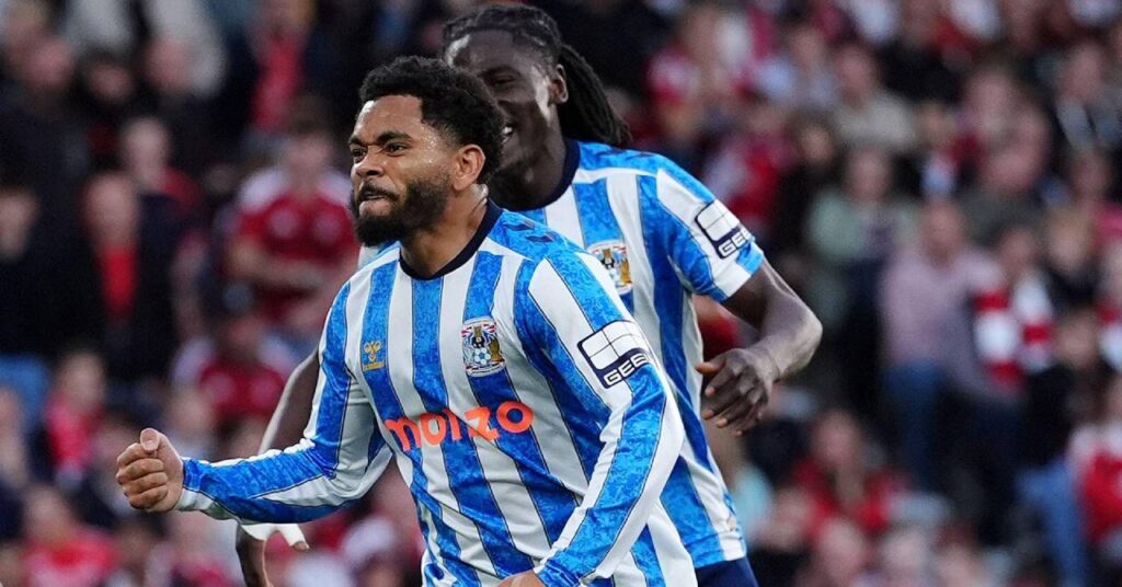 Wales footballer Jay Dasilva clenching his right fist to celebrate a goal while playing for Premier League team Coventry City Football Club in a blue and white striped shirt with the club badge and Hummel logo on the chest