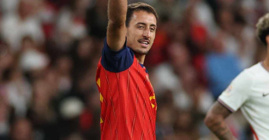 La Liga team Real Sociedad footballer Mikel Oyarzabal raising his right arm to celebrate a goal while playing for the Spain national football team in a red shirt with blue trim and yellow stripes