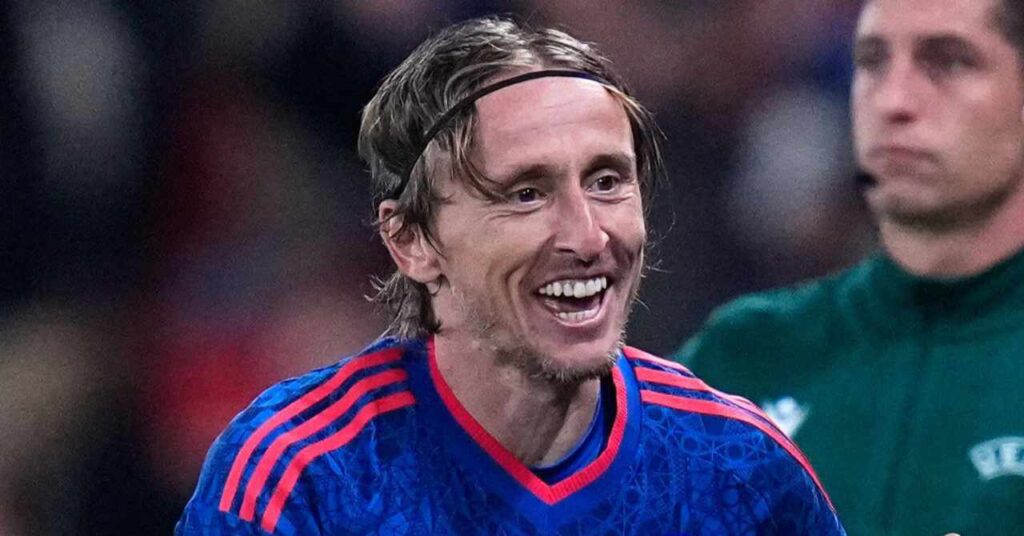 AC Milan footballer Luka Modric smiling to celebrate a goal while playing for the Croatia national football team in a blue shirt with red Adidas trim on the shoulders and neck