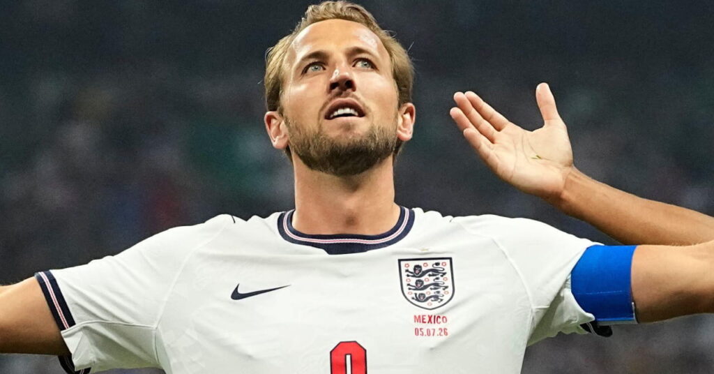 Footballer Harry Kane spreading his arms and looking upwards during the World Cup 2026 while wearing the England national team football kit of a white shirt with blue trim and his number in red on the shirt with dark blue shorts and white trim featuring the England badge and his number in white