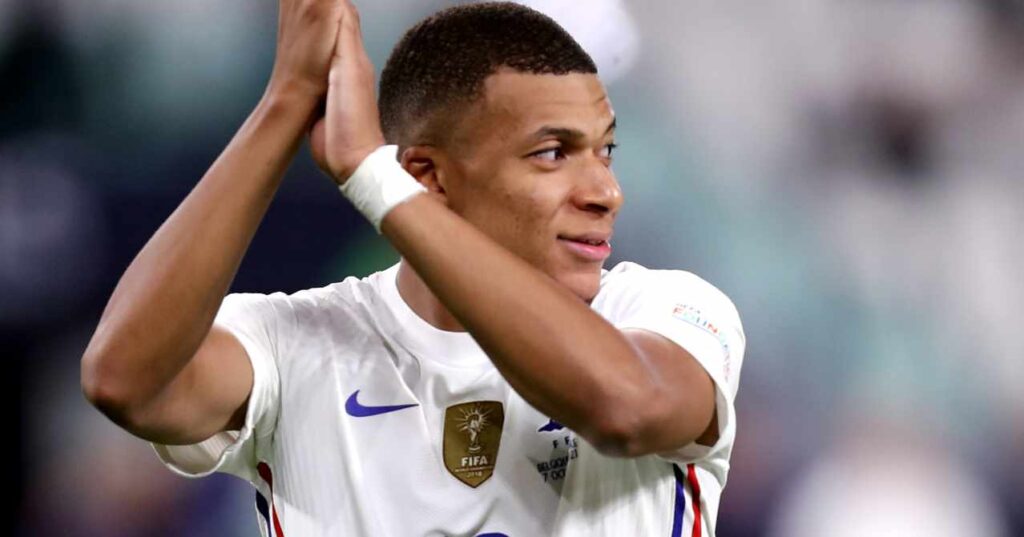 La Liga team Real Madrid Football Club footballer Kylian Mbappe looking to his left and applauding while playing for the France national team in a white shirt with a white band on his left wrist