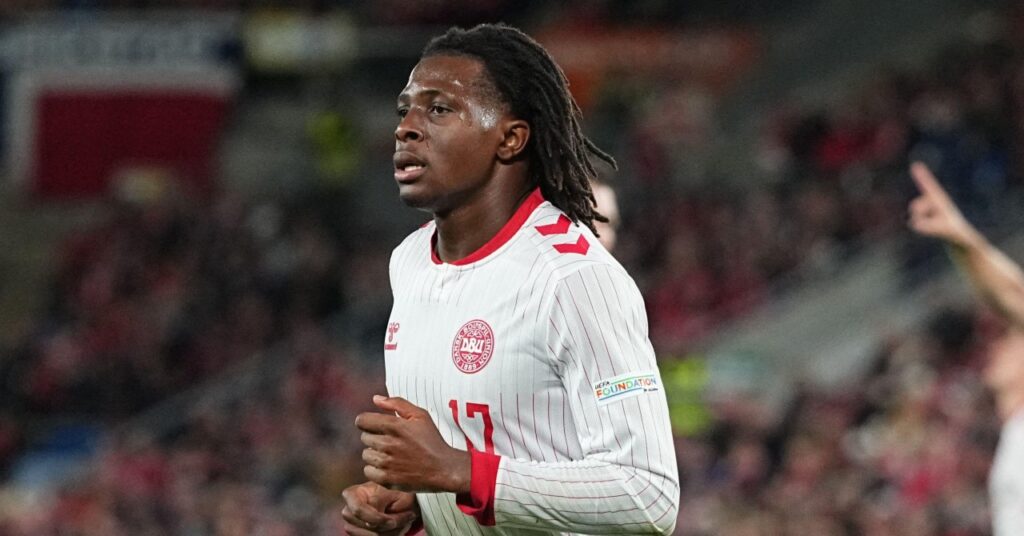 Premier League team Manchester United Football Club footballer Patrick Dorgu running to his right while playing for the Denmark national team in a white shirt with red Hummel trim and the sportswear brand and national team logo in red on the chest alongside the number 17