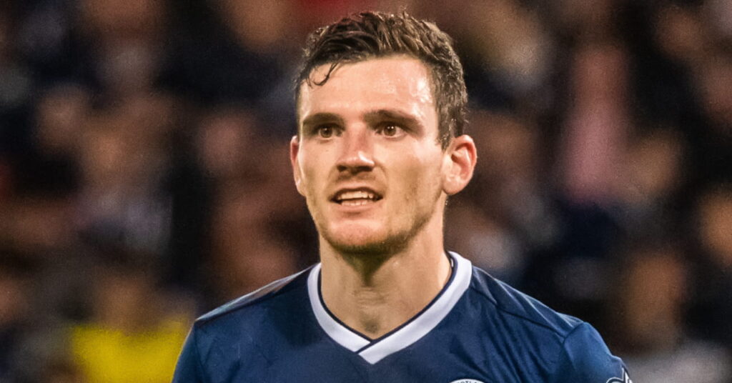Footballer Andy Robertson playing in a stadium while wearing the Scotland national team football shirt of a dark blue top with a white collar and the national flag in yellow on the chest. Robertson is looking to his right